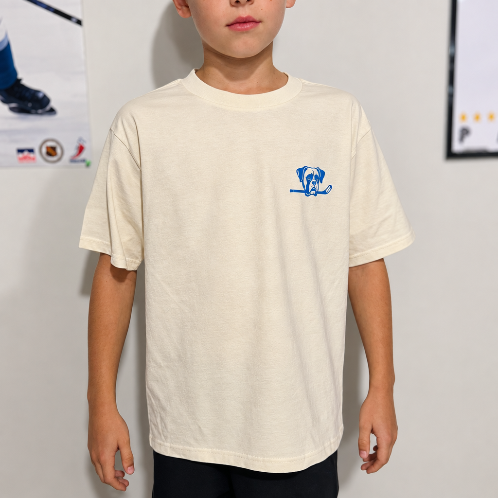 Youth model wearing the Light Sand Youth Hockey T-Shirt, front view, with hockey posters in the background